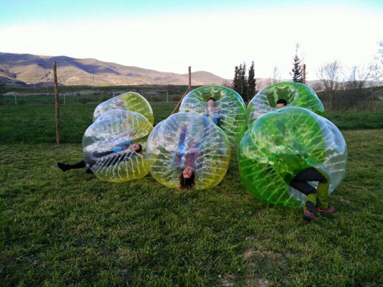 personas jugando dentro de unas pelotas gigantes sobre el césped